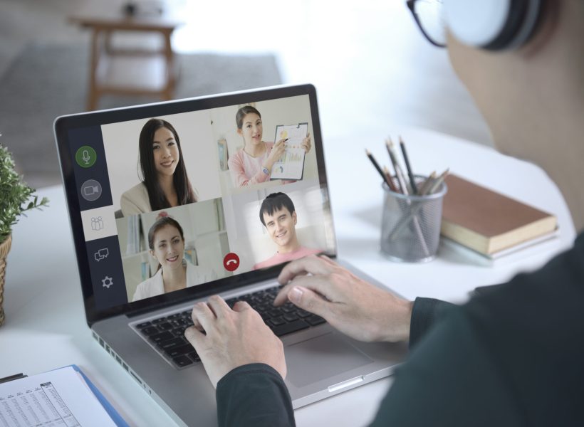 Young Asian businessman wear headphones working remotely from home and virtual video conference meeting with colleagues business people. social distancing at home office concept.